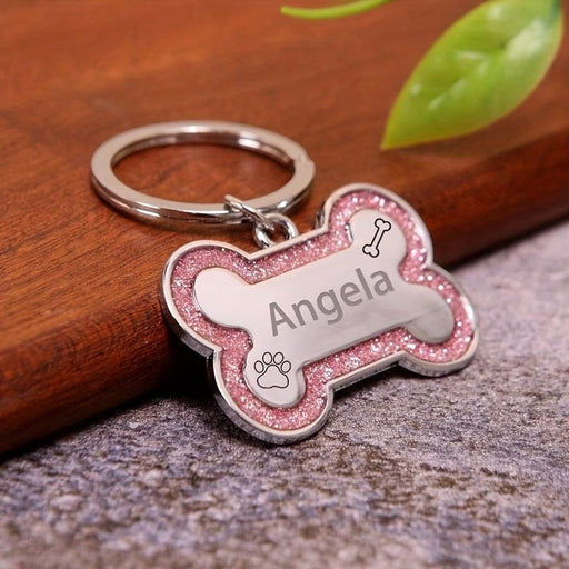 Blessing Sells personalized pink glitter bone-shaped pet ID tag with 'Angela' engraved and a paw print.