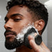 Blessing Sells black hexagonal facial cleansing brush with bristles, used by a man with a beard to exfoliate and deep clean his face.